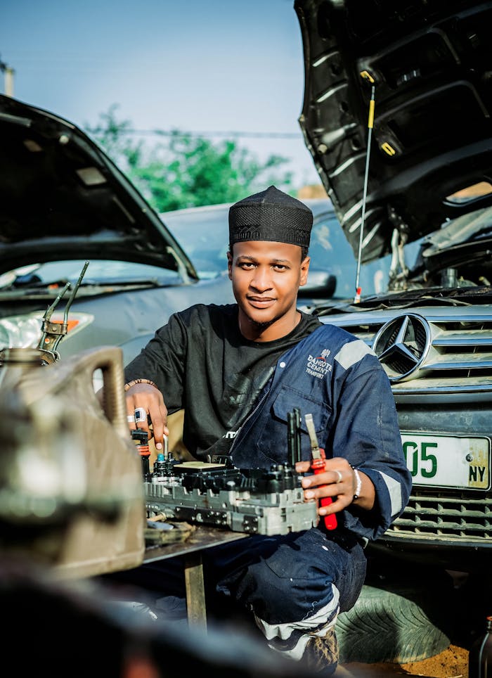 Young mechanic wearing uniform repairs a car outdoors, showcasing expertise in automotive service.