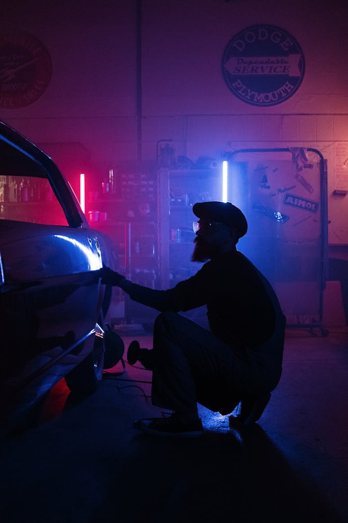Silhouette of mechanic repairing a car in a dimly lit garage with colorful neon lights.